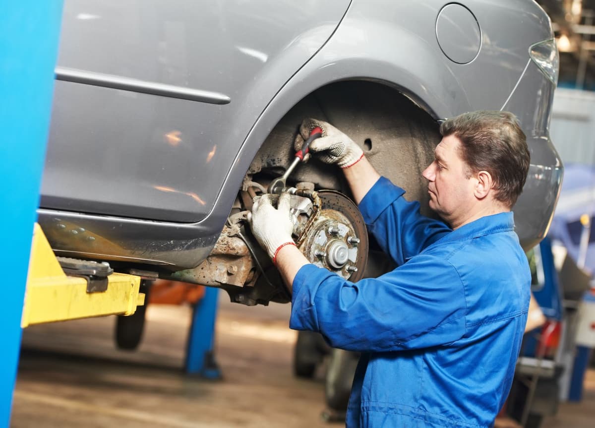 A mechanic working on the rear brake of a car raised on a hoist.
