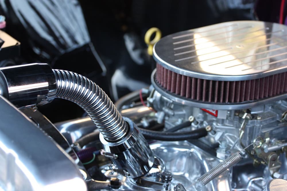 A close view of an engine with a chrome air cleaner and hose.